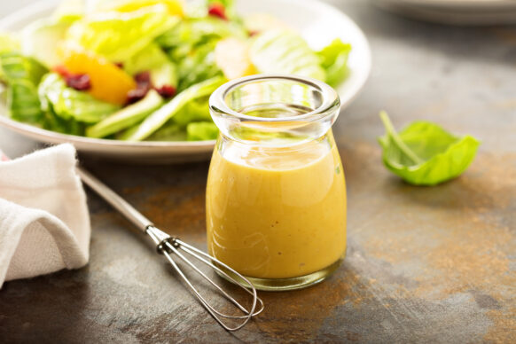 Mustard dressing in a small glass container with a salad in the background