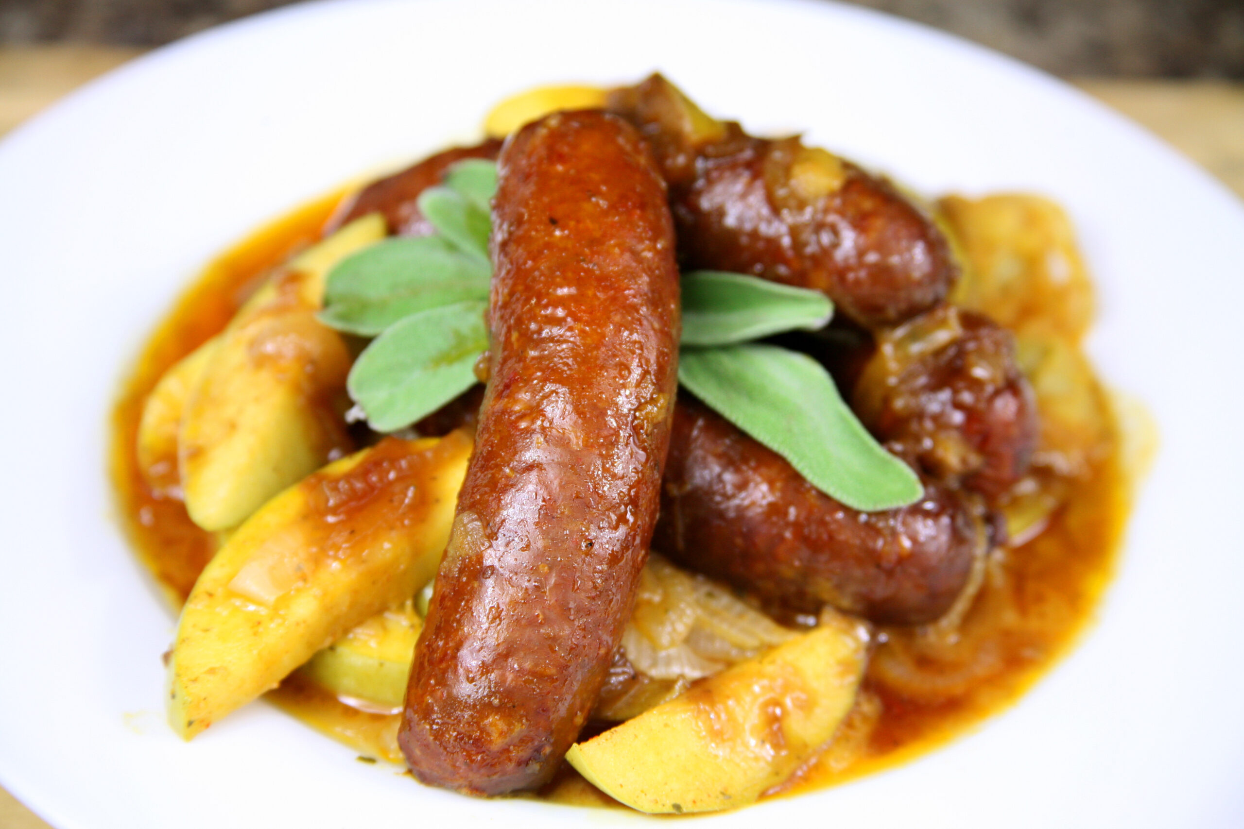 Sausages on a plate of sauce with apples and onions