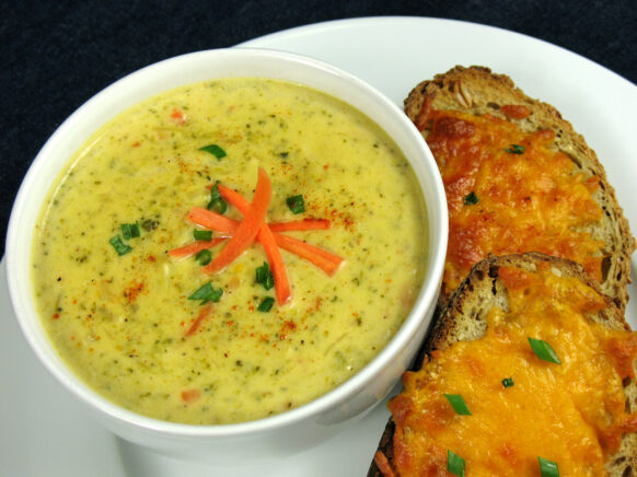 Bowl of Cheddar Broccoli soup with pieces of cheesy bread