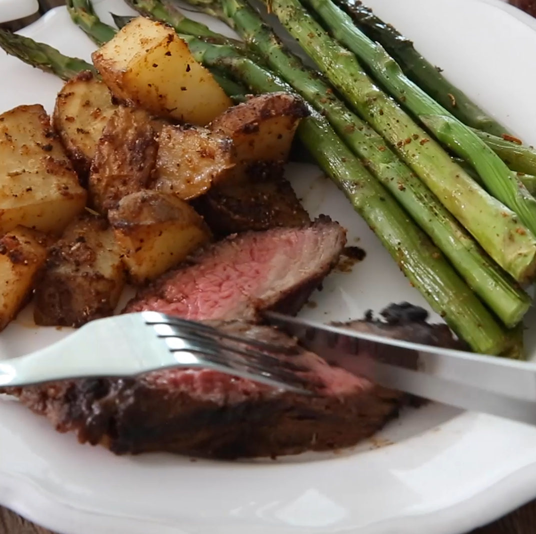 Steak being cut on a plate with potatoes and asparagus